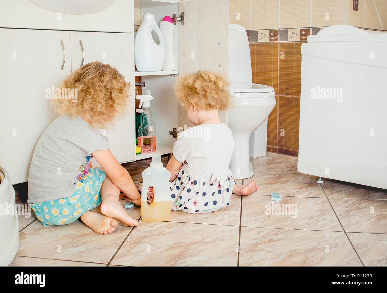 Unattended children play quietly at bathroom with dangerous household chemicals. Safety hazard at home concept. Keep away from children`s reach. Stock Photo